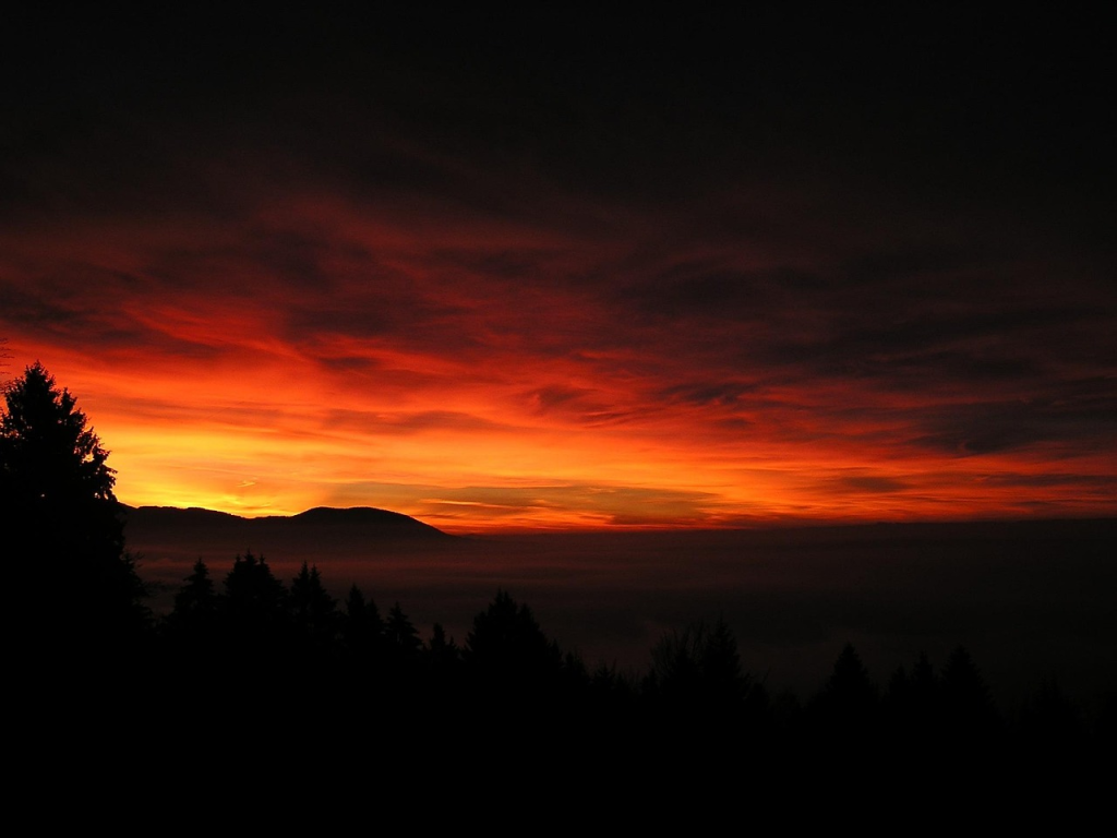 Landscape at dusk featuring a sunset in yellow, orange, red, and deep burgundy reflected in the clouds. 